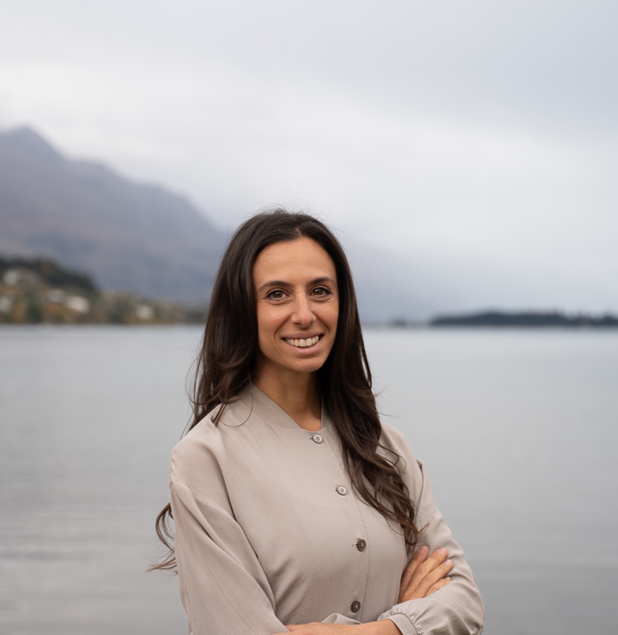Fiona Laryn standing by Lake Wakatipu with the Queenstown mountains behind her